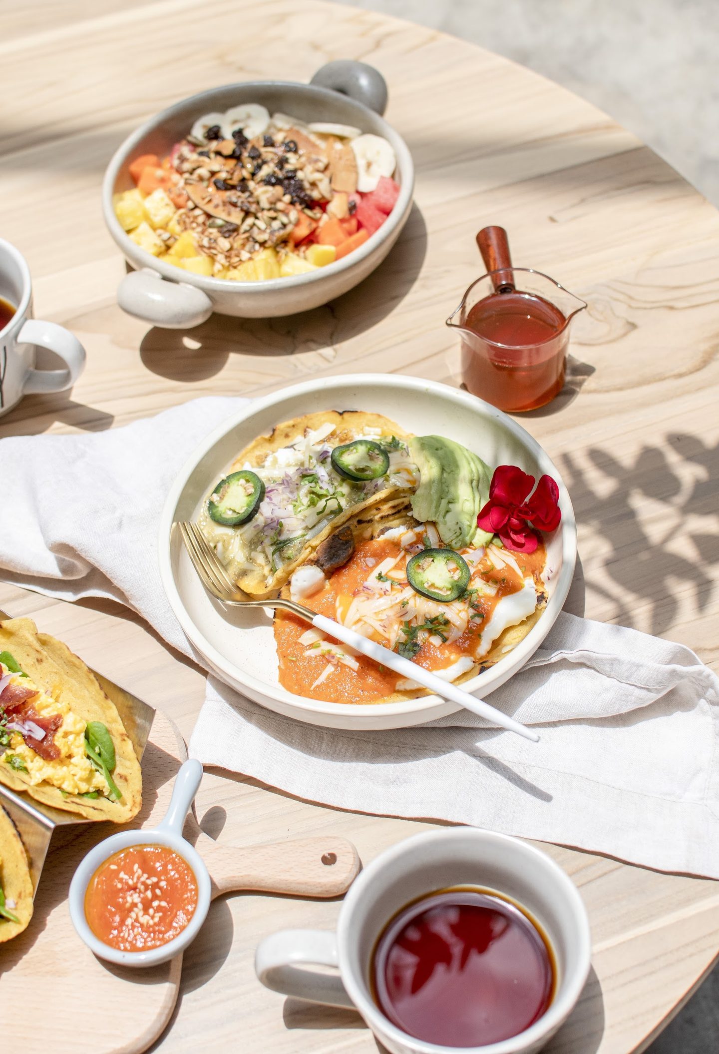 Mesa de brunch al sol con chilaquiles, bowl de granola y café