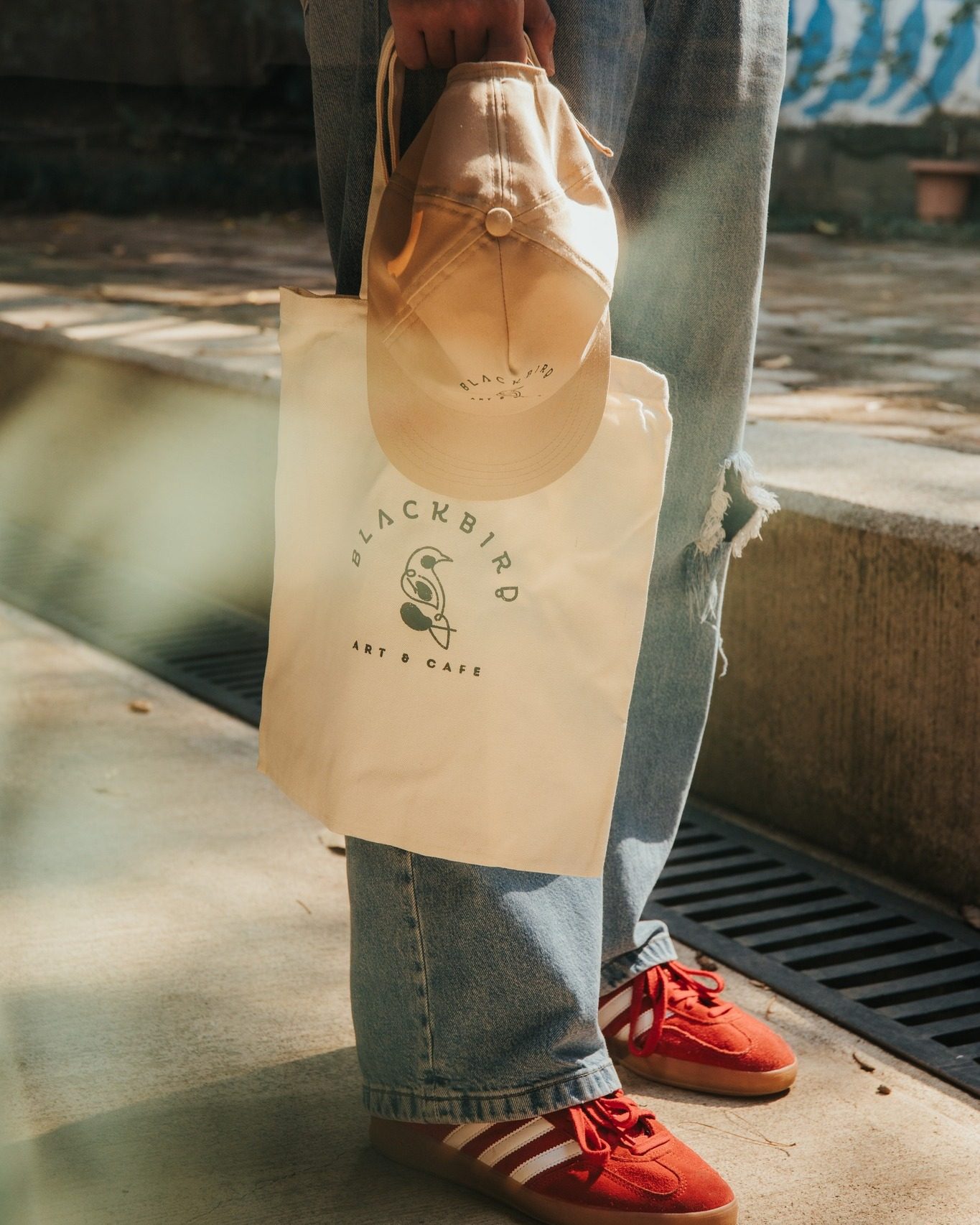 Persona sosteniendo la bolsa de tela y la gorra con el logo de Blackbird a contraluz